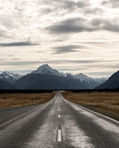 An asphalt road leading to the snow-covered Mount Cook.