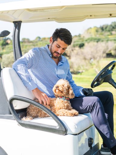 A young Caucasian male in a golf cart with his Goldendoodle puppy on a professional golf course