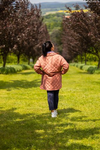 A vertical of a female in a coat, walking on green grass in a park