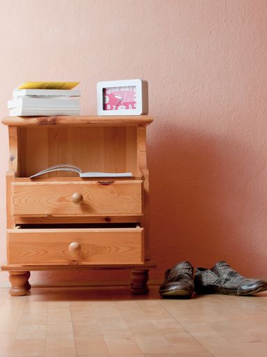 A vertical shot of a drawer with books and a clock on top next to a pair of shoes