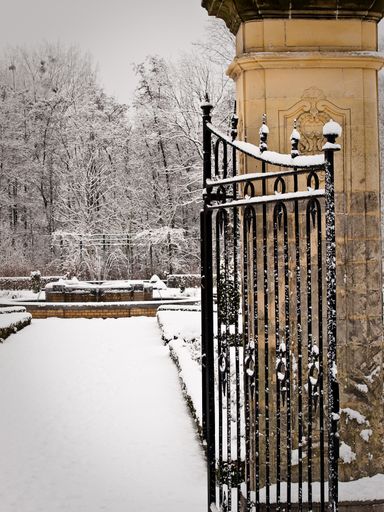 A vertical shot of a gate of a park covered in snow during winter