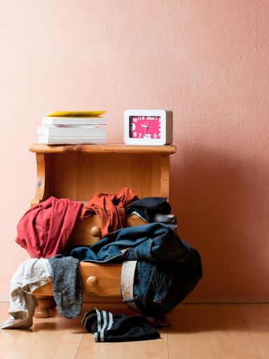 A vertical shot of a drawer with several clothes on it together with books and a clock