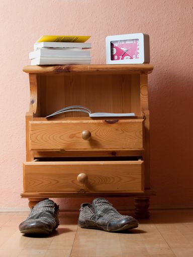 A vertical shot of a drawer with books and a clock on it with a pair of shoes in front