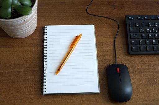 A shot of office table with notebook, pen, keyboard and mouse