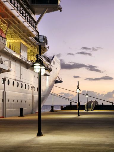 A vertical shot of a marine vessel docked at a dock, the sun setting in the background