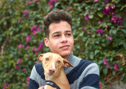 A portrait of a happy Hispanic male with his brown dog in the park