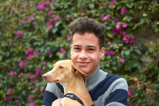 A portrait of a happy Hispanic male with his brown dog in the park