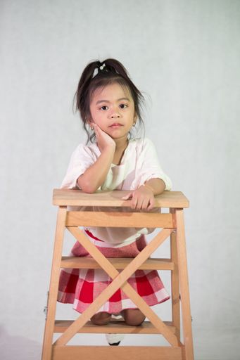 A vertical shot of a cute  Southeast Asian little girl leaning on the table on the white background