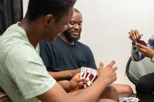 A group of diverse friends gathered around a wooden table to play a game of cards, laughing and enjoying each other's company
