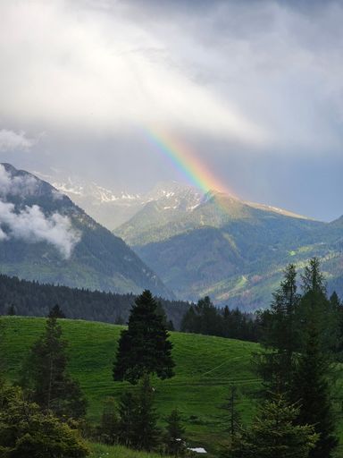A scenic view of a rainbow over green Dolomites mountains