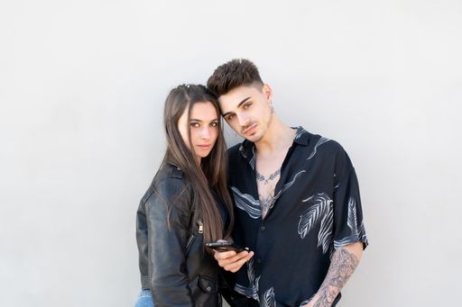A beautiful shot of a Caucasian couple looking at the camera while holding a phone isolated on a white background