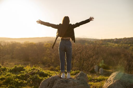 A scenic shot of a woman wearing a leather jacket with her arms open in the field