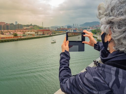 A closeup of a female taking a photo of a sailboat sailing on the river through her mobile phone