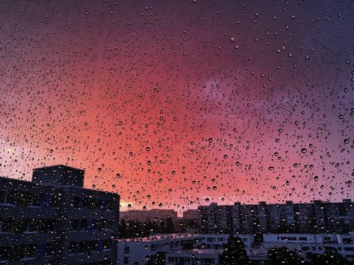 A closeup of a rain-streaked window at pink sunset