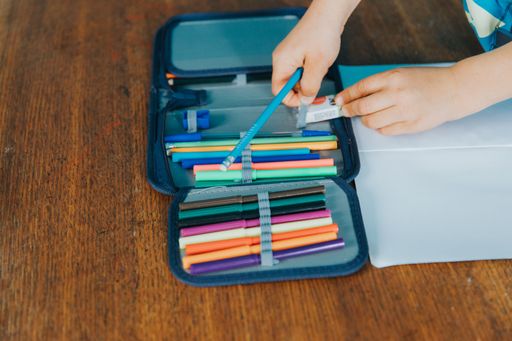 A young child using colorful pencils to draw on a white sheet of paper