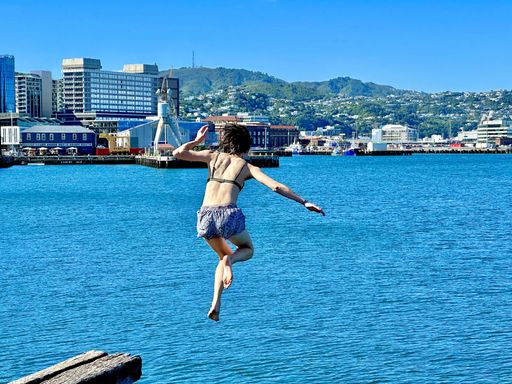 A young woman in a bikini jumps into the crystal clear water from a pier