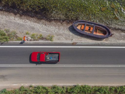 An aerial shot of vehicle running along the street with an unused raft on the side of a road