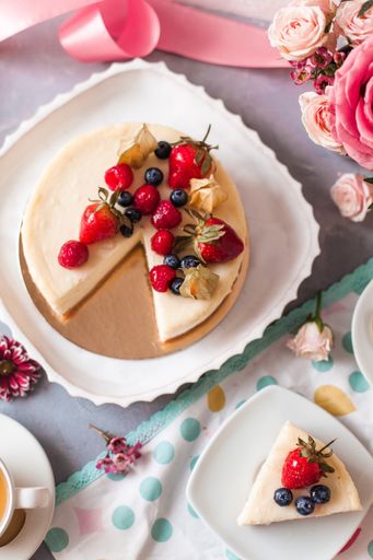 An aesthetic shot of a cheesecake with berries served with tea and arranged with flowers