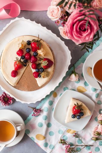 An aesthetic shot of a cheesecake with berries served with tea and arranged with flowers