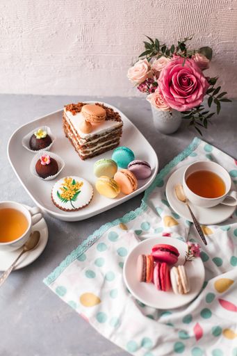 A closeup of tasty sweets on the table served with a tea cup and arranged with flowers