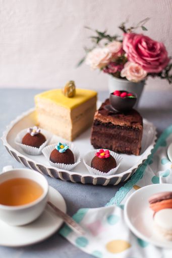 A closeup of tasty sweets on the table served with a tea cup and arranged with flowers
