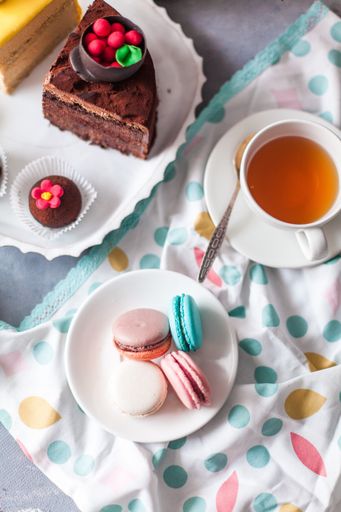 A top view closeup of a variety of cake pieces and macaroons  on the white plate on the grey table