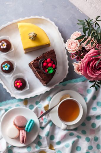 A top view closeup of a variety of cake pieces and macaroons  on the white plate on the grey table