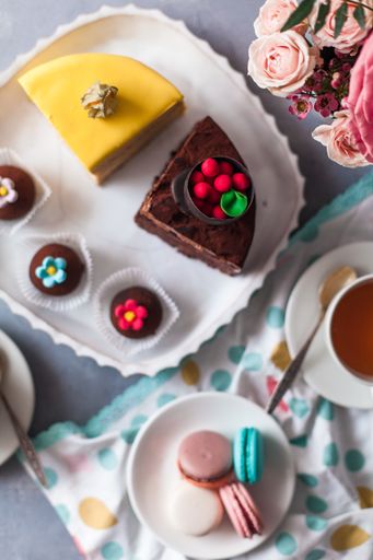 A top view closeup of a variety of cake pieces and macaroons  on the white plate on the grey table