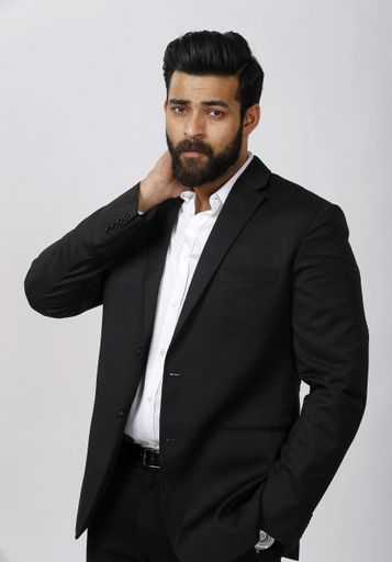 A vertical shot of an attractive male posing in a black suit with one hand on his neck with a white background.