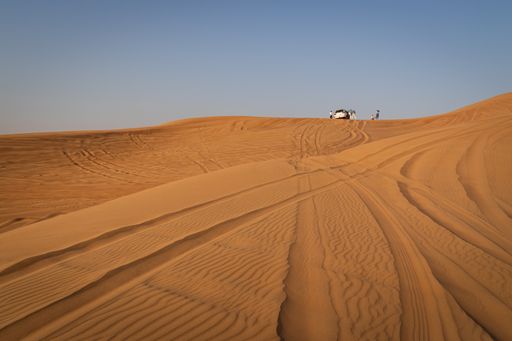 A four-wheel-drive desert safari car on a sand dune with tourists