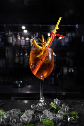 A glass of craft cocktail with ice cubes, lemon slices, and garnish against the backdrop of a bar