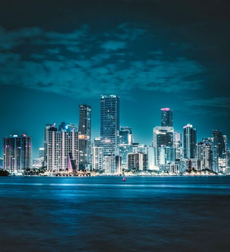 An idyllic scene of a bustling city skyline in front of a tranquil body of water, with a few boats gently bobbing in the waves
