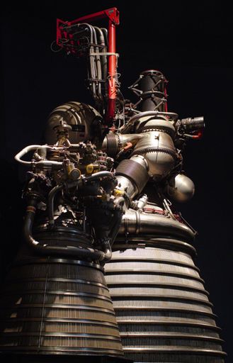 An isolated image of a small engine mounted on the top of a large rocket booster, with a black background and white highlights