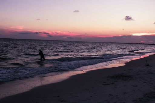 A silhouette of a man fishing in the ocean at Mexico Beach, Florida during sunset.