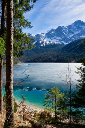 A scenic view of a tranquil lake surrounded by lush green trees and snow-capped mountains.