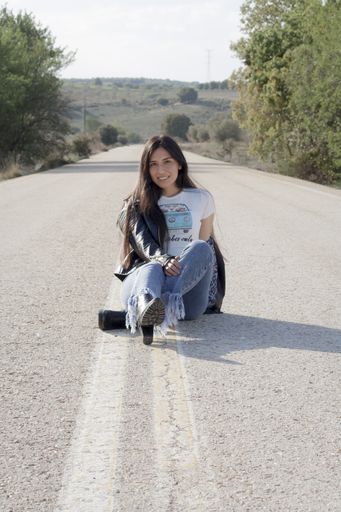A young Latina female wearing jeans, bodysuit and leather jacket and posing on an asphalt road
