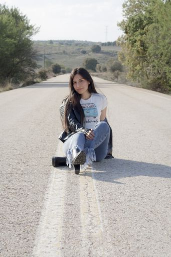 A young Latina female wearing jeans, bodysuit and leather jacket and posing on an asphalt road