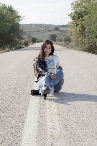 A young Latina female wearing jeans, bodysuit and leather jacket and posing on an asphalt road