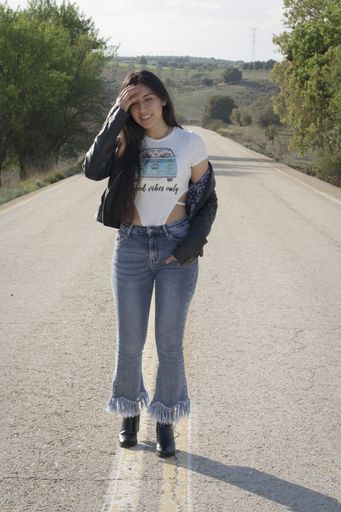 A hot young Latina female wearing jeans, bodysuit and leather jacket and posing on an asphalt road