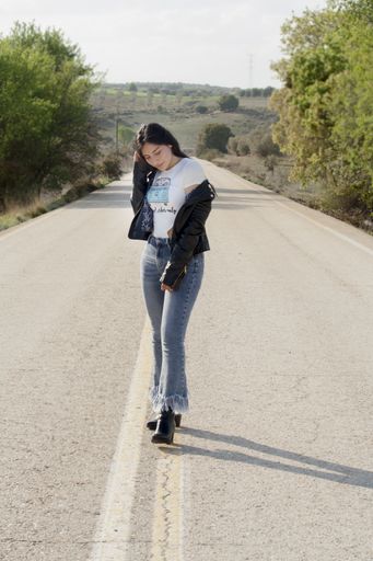A hot young Latina female wearing jeans, bodysuit and leather jacket and posing on an asphalt road
