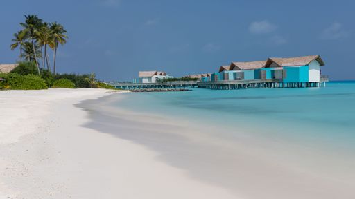 An idyllic beach featuring a row of blue cabins situated in the tranquil turquoise waters