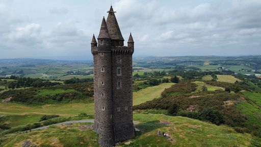 An aerial view of the Scrabo tower situated atop a rolling grassy hill in Ireland