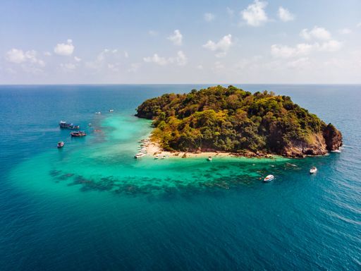 An aerial shot of a small green island in the middle of the ocean with beautiful clouds in the background