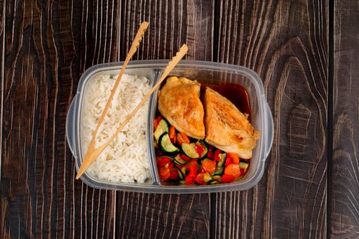 A top view of chicken stir fry with vegetables and steamed rice in a plastic lunchbox