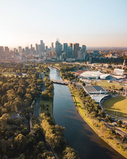 A drone vertical shot of the Melbourne cityscape with a river and green trees on a sunny day