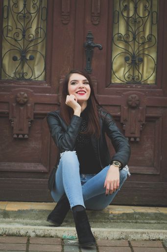 A young caucasian brunette female in a leather coat posing while sitting in front of an old door