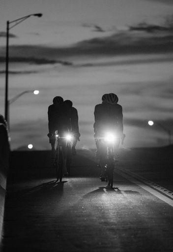 Two individuals are engaging in a leisurely bike ride at night, illuminated in the dark by the light of their bicycles