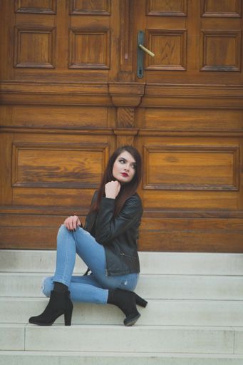 A vertical shot of a young brunette female posing in front of the wooden door of a building