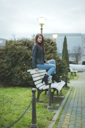 A beautiful Caucasian female with red lipstick and leather jacket sitting on a park bench