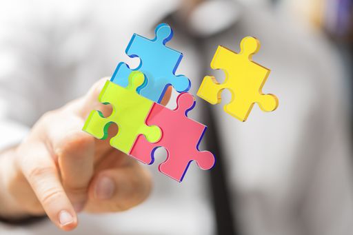 Multicolored pieces of a jigsaw puzzle behind a person's fingers